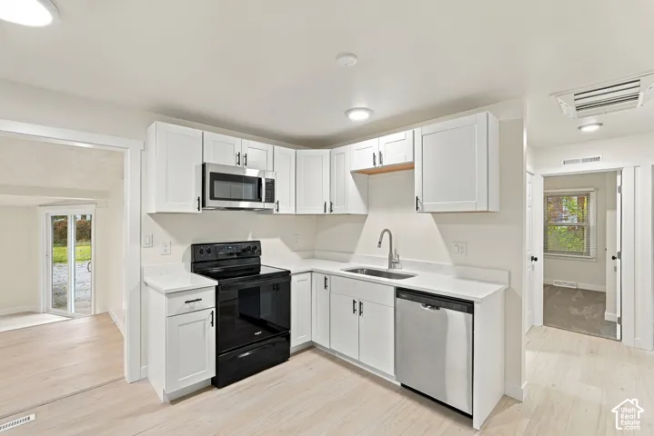Kitchen featuring white shaker-style cabinetry, white countertops, a stainless steel dishwasher, a built-in stainless steel microwave, and wood-finish flooring