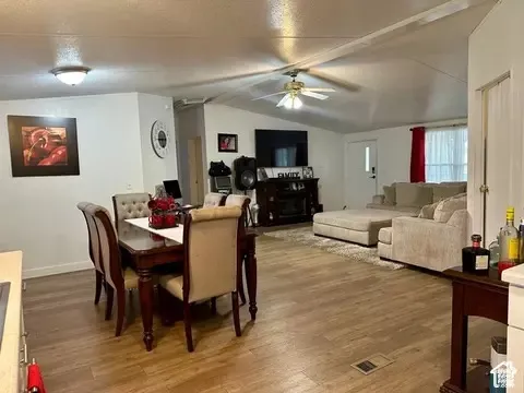Open-concept interior featuring wood-finish flooring, vaulted ceilings, and a central ceiling fan with integrated lighting