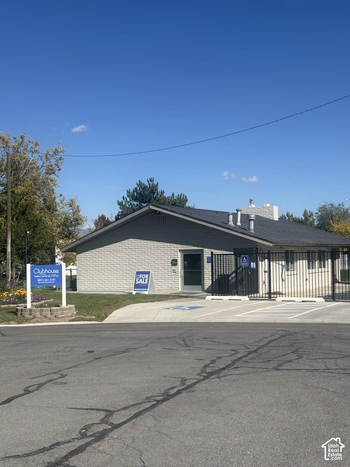 Single-story building featuring brick masonry exterior, asphalt shingle roof, paved parking area, and metal perimeter fencing