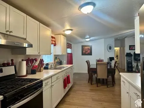 Kitchen featuring white shaker-style cabinetry, wood-finish flooring, stainless steel range hood, dual-basin sink, and recessed ceiling lighting
