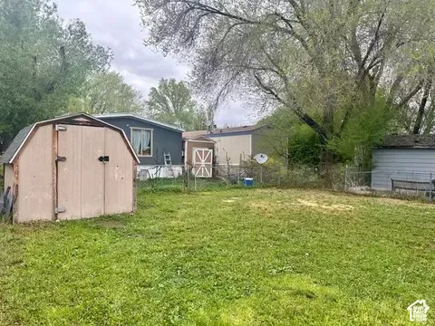 Expansive backyard featuring a lawn, mature trees, chain-link fencing, and two detached storage structures