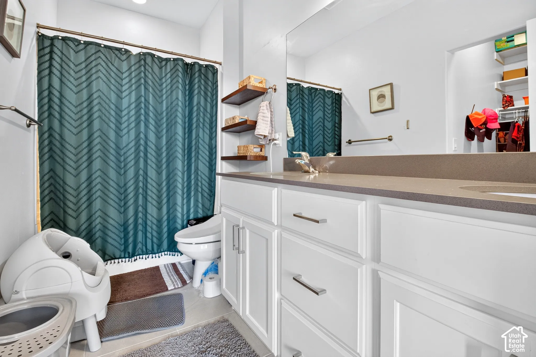Bathroom featuring a solid-surface countertop, white shaker-style vanity cabinetry with brushed nickel hardware, a large wall-mounted mirror, and tiered wood wall shelving