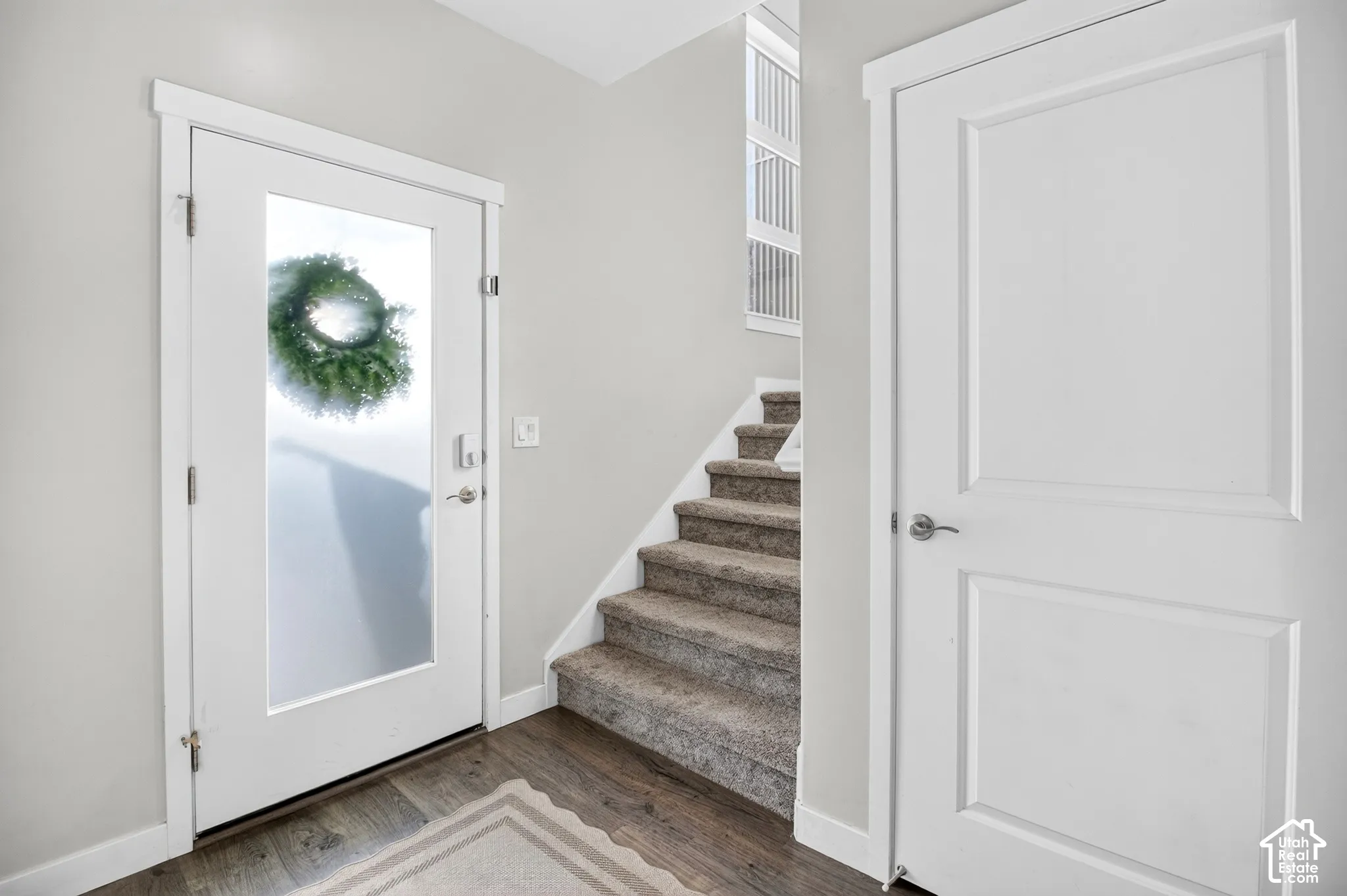 Entryway featuring a solid door with a frosted glass panel, wood-finish flooring, carpeted stairs, and two-panel interior doors with satin nickel hardware