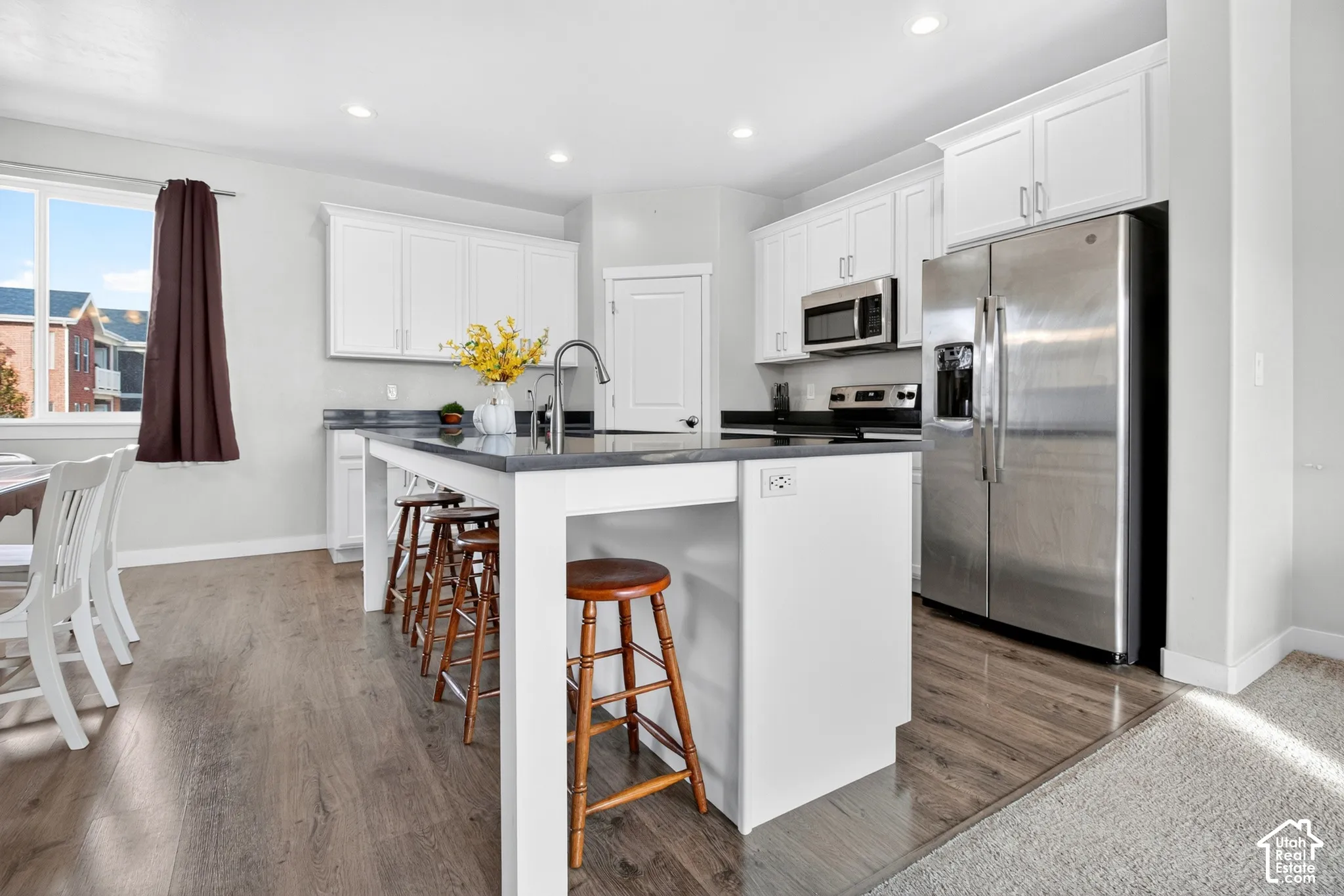 Kitchen featuring white shaker-style cabinetry, dark stone countertops, a center island with a stainless steel faucet, and stainless steel appliances including a side-by-side refrigerator and microwave