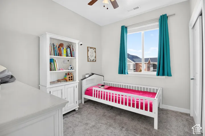 Neutral-toned room featuring plush carpeting, a large picture window, and a ceiling fan