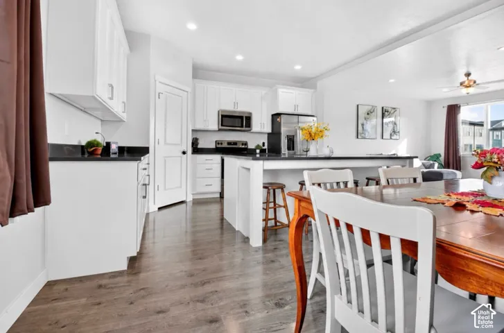 Kitchen featuring white cabinetry, dark countertops, wood-finish flooring, recessed lighting, and a central island with an integrated breakfast bar