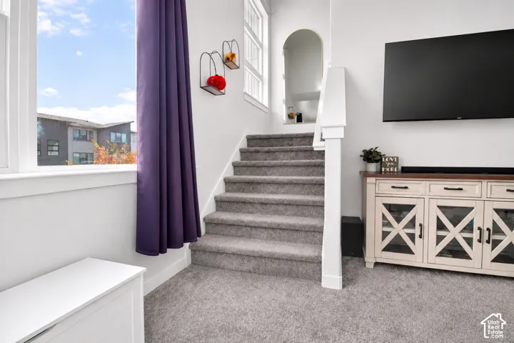 Carpeted staircase featuring a white post-and-rail balustrade, arched wall niche, and natural light from tall, multi-pane windows