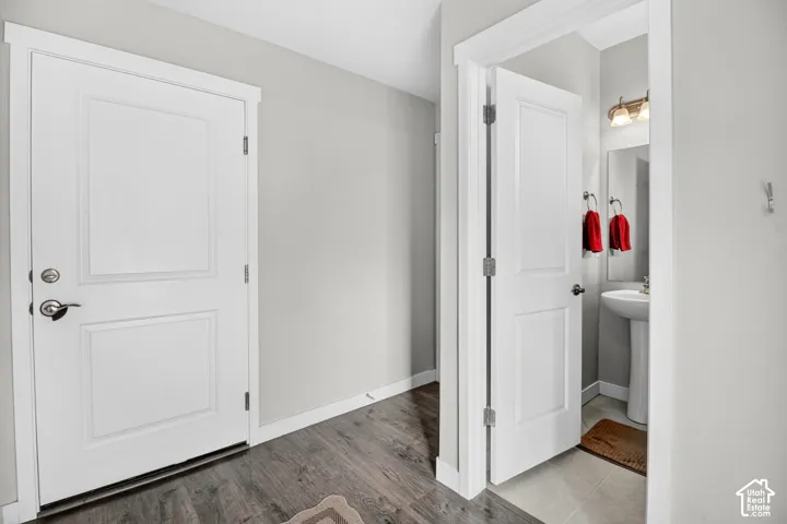 Entryway featuring wood-finish flooring, two-panel interior doors with metallic hardware, neutral wall paint, and a pedestal sink fixture