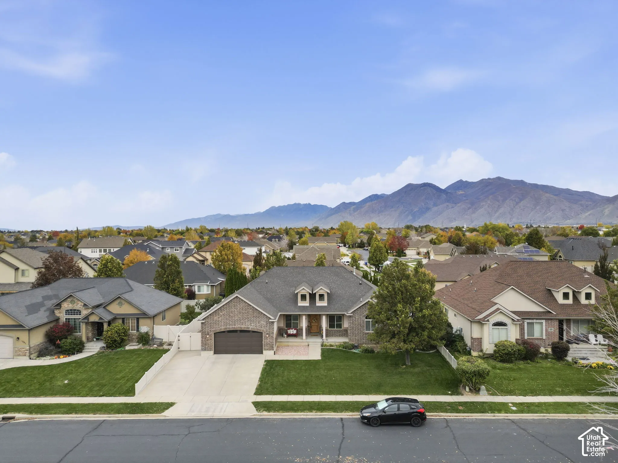 Brick exterior residence featuring an asphalt shingle roof, two dormer windows, a paved driveway, and an attached multi-car garage, set against a backdrop of mountain scenery
