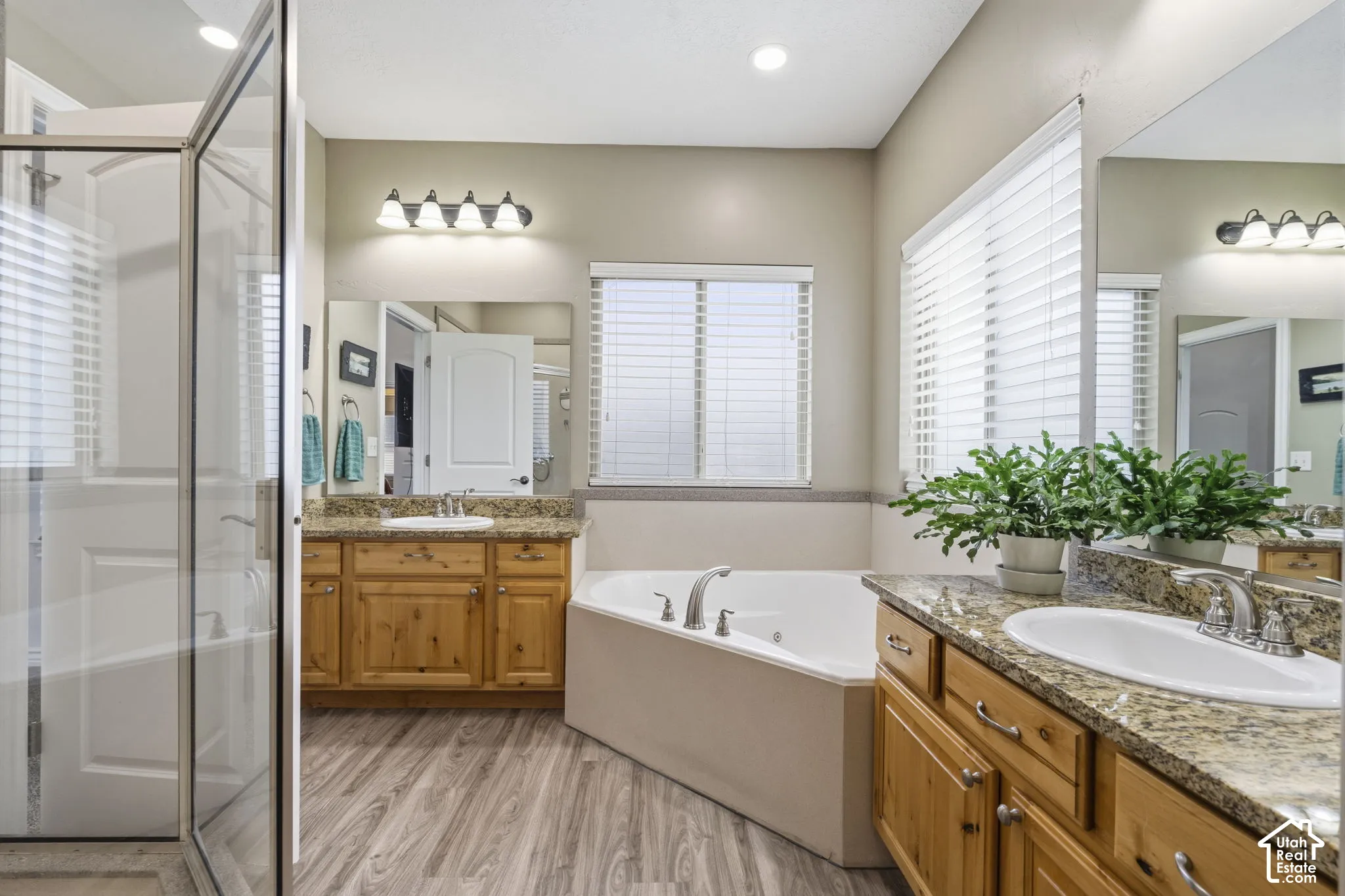 Bathroom featuring dual wood-finish cabinetry, granite countertops with undermount sinks, a corner soaking tub, and a glass-enclosed shower