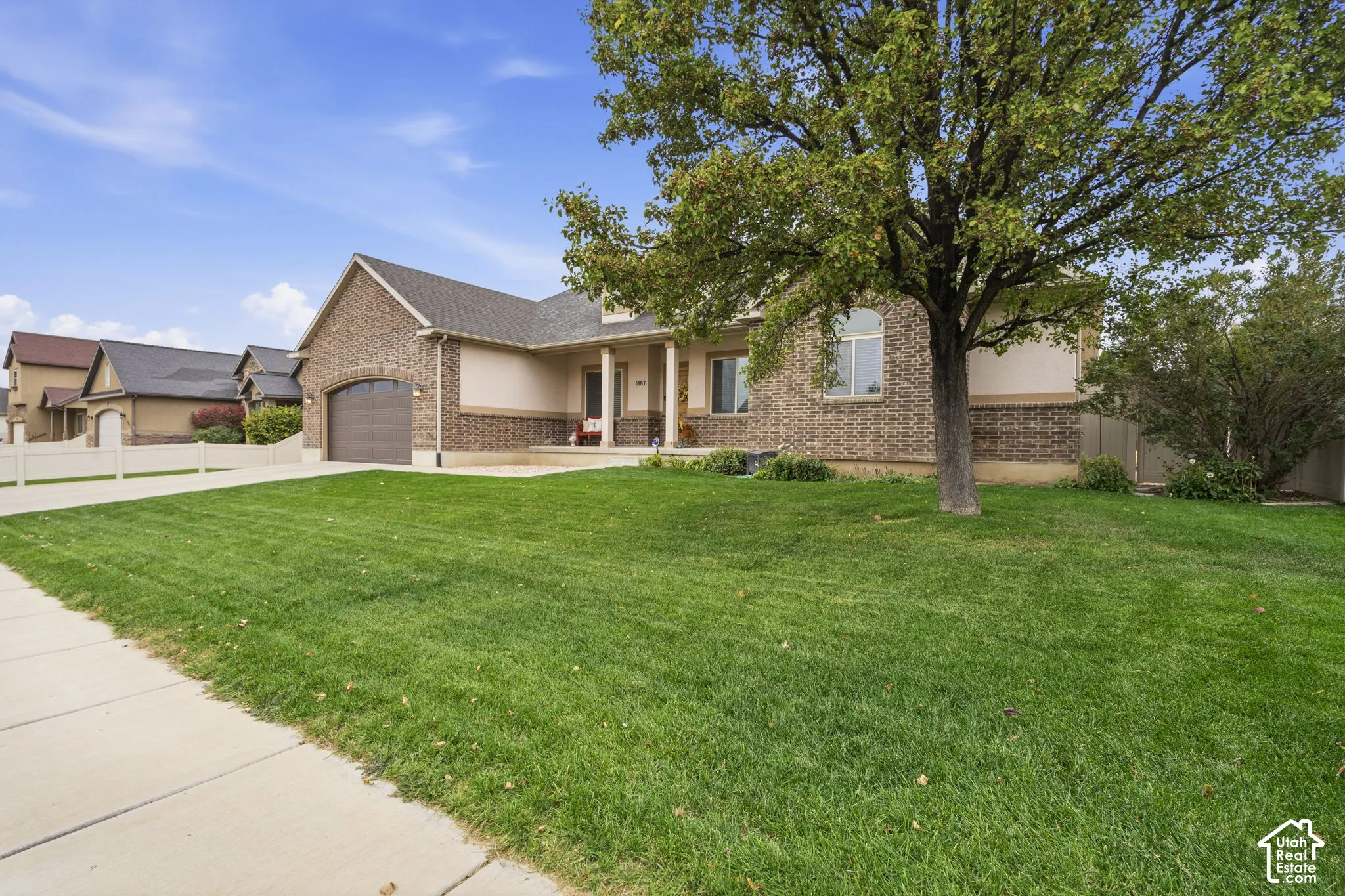 Brick and stucco exterior featuring a covered front porch with columns, an attached garage, and a expansive front lawn with mature trees
