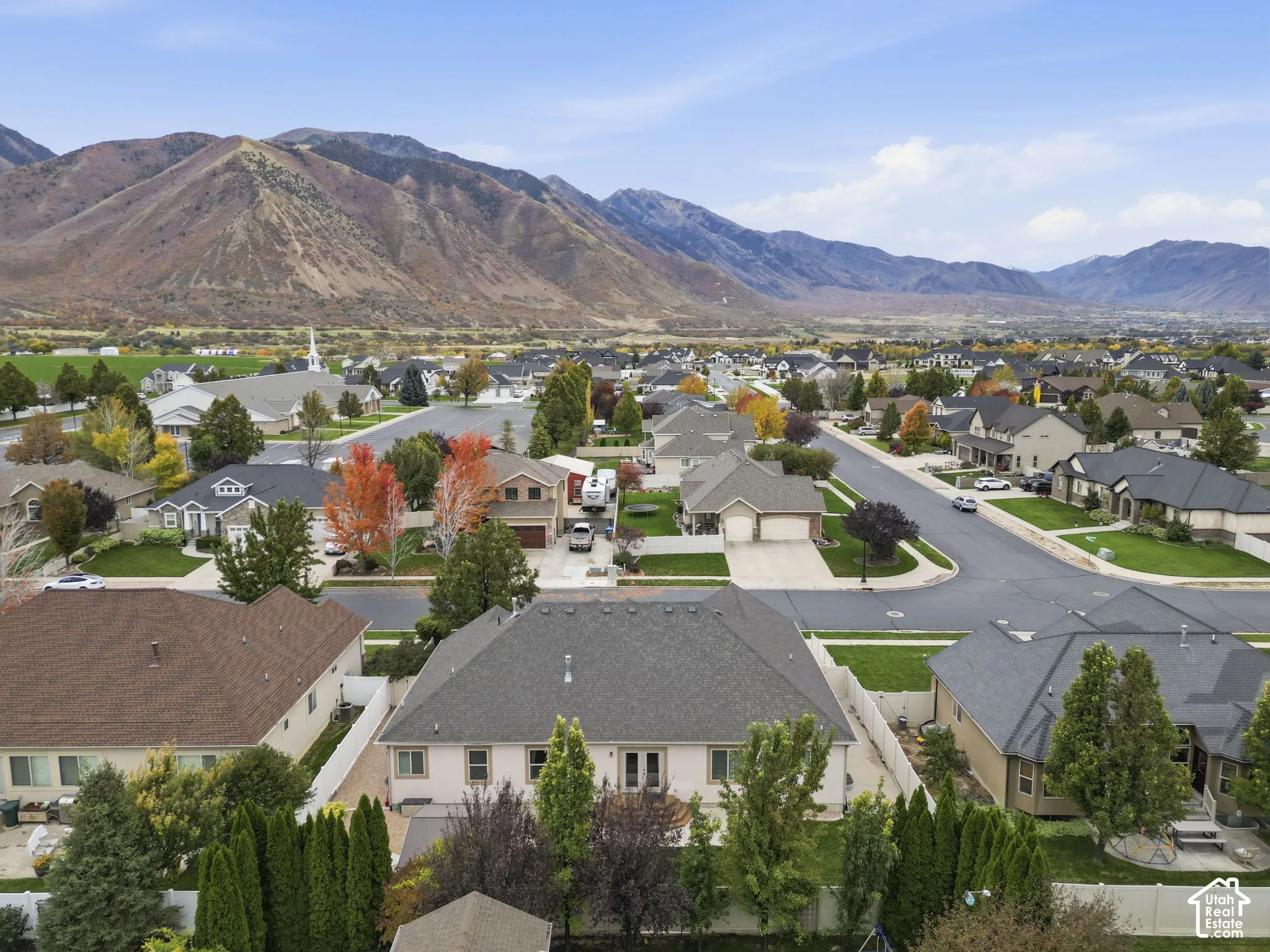 Aerial perspective featuring a residential lot with mature landscaping, perimeter fencing, and prominent mountain backdrops