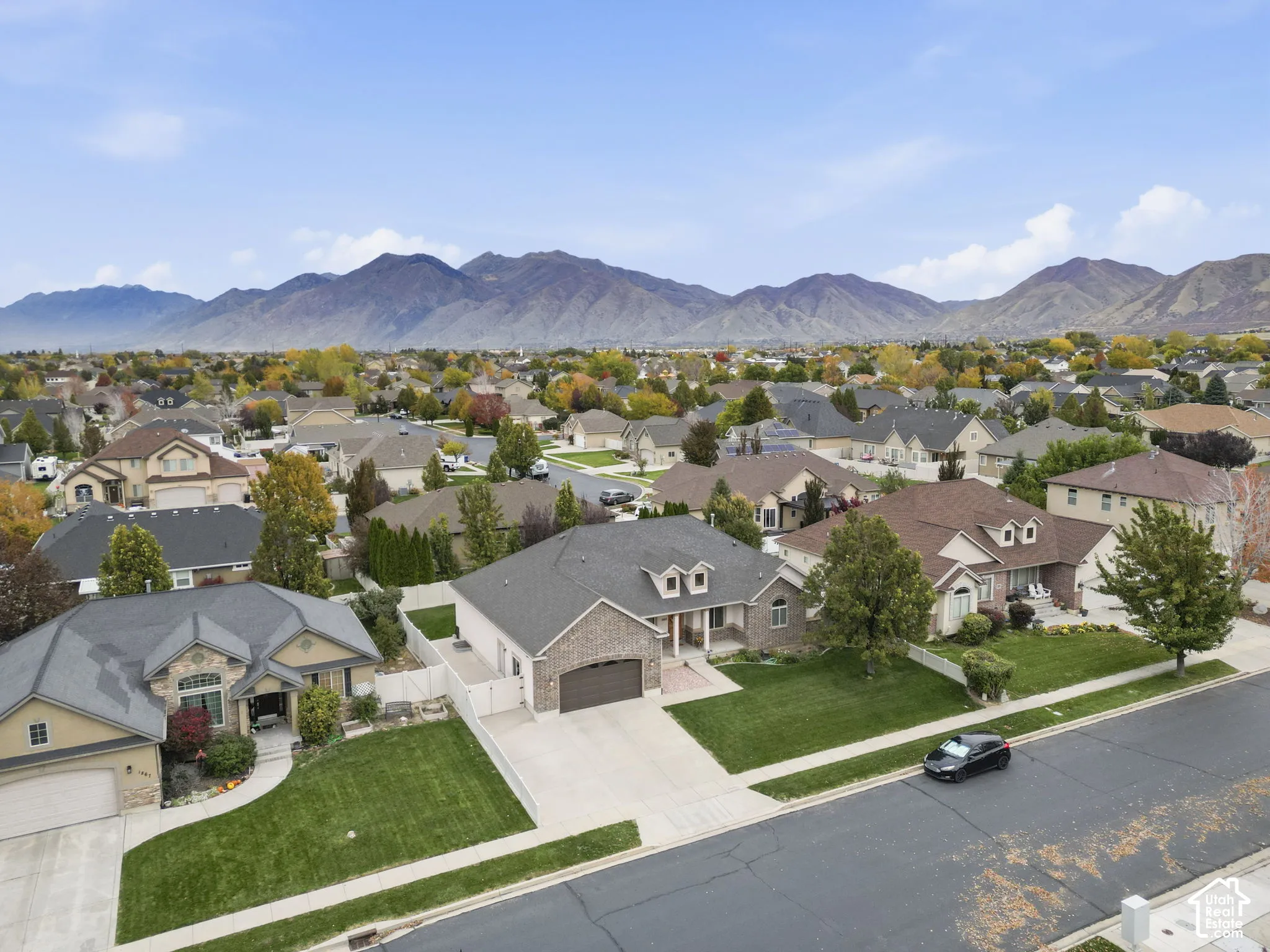 Aerial perspective of residential properties featuring stone and stucco exteriors, attached garages, manicured lawns, and a prominent mountain backdrop