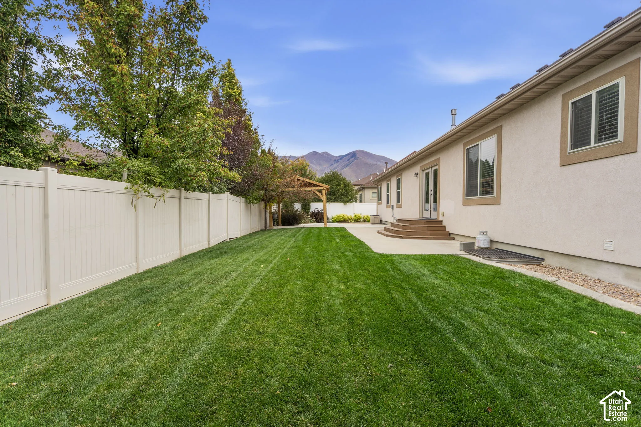 Backyard featuring a manicured lawn, privacy fencing, concrete patio, wooden pergola, and mountain backdrop