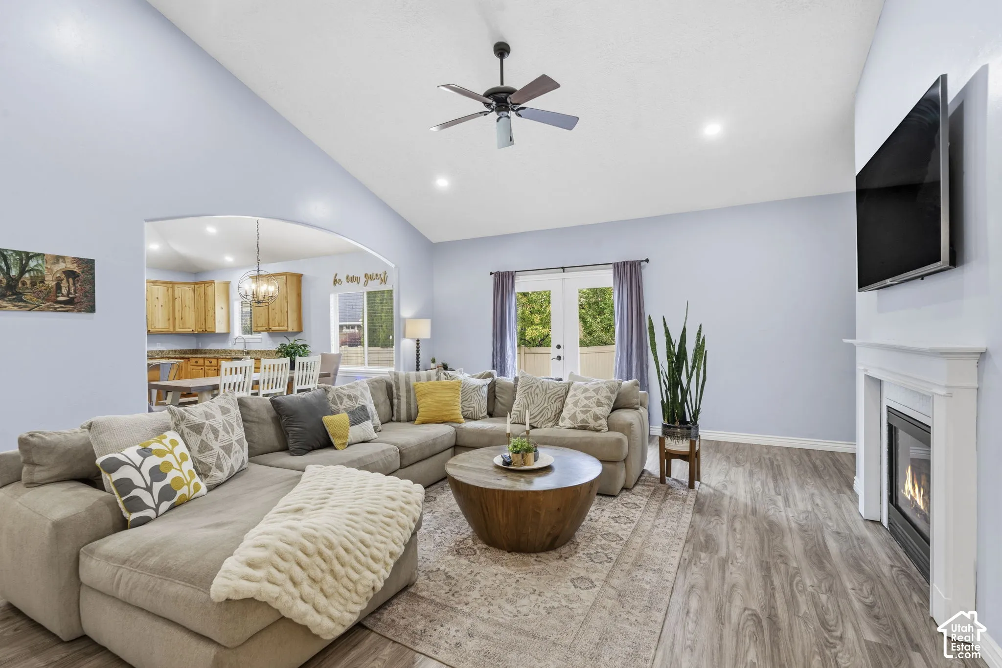 Vaulted ceilings, wood-finish flooring, fireplace with a white mantel, ceiling fan, and double-door access to the exterior