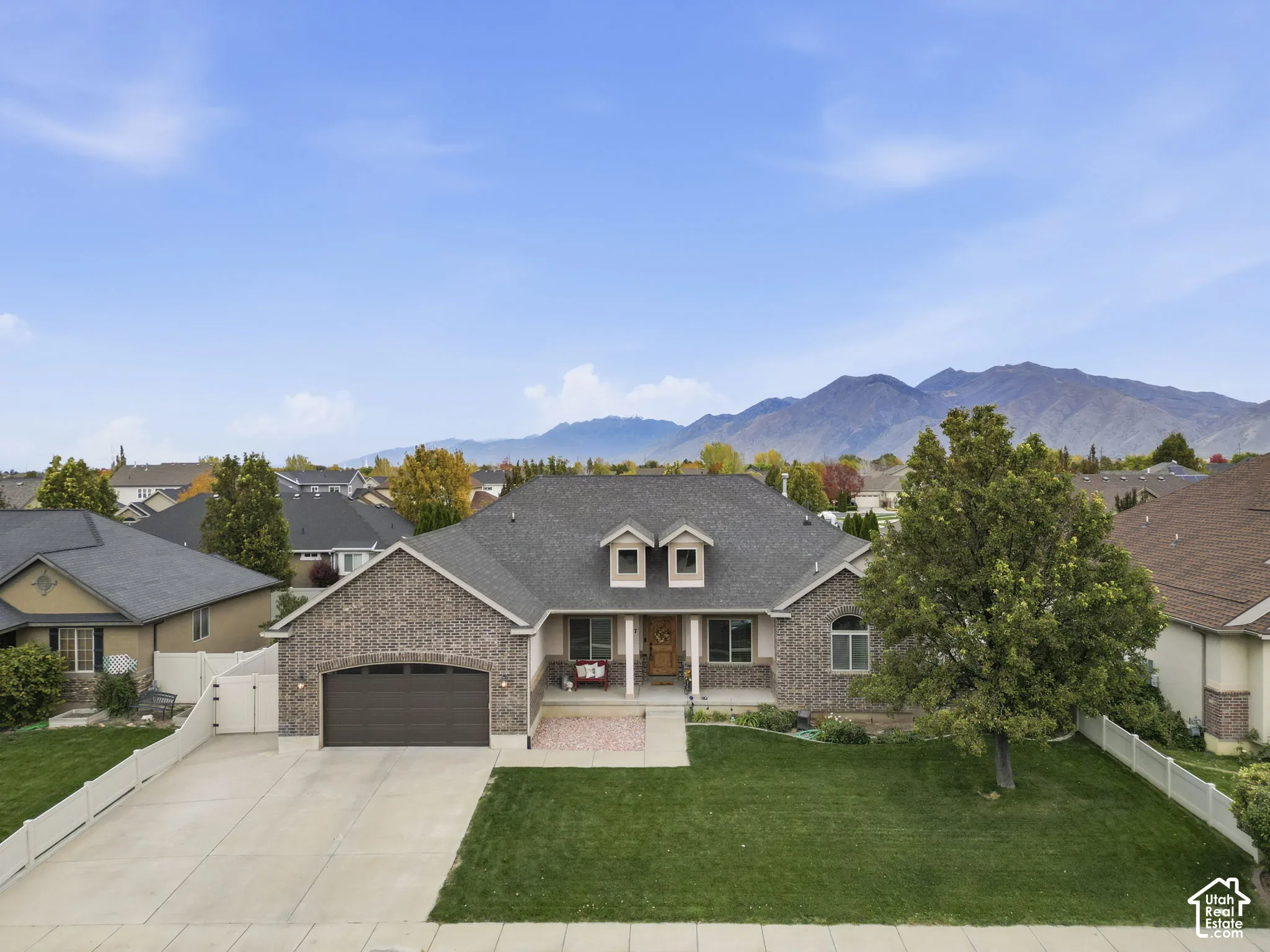 Single-story brick exterior featuring a multi-gabled roofline, dual dormer windows, attached two-car garage, and mountain backdrop