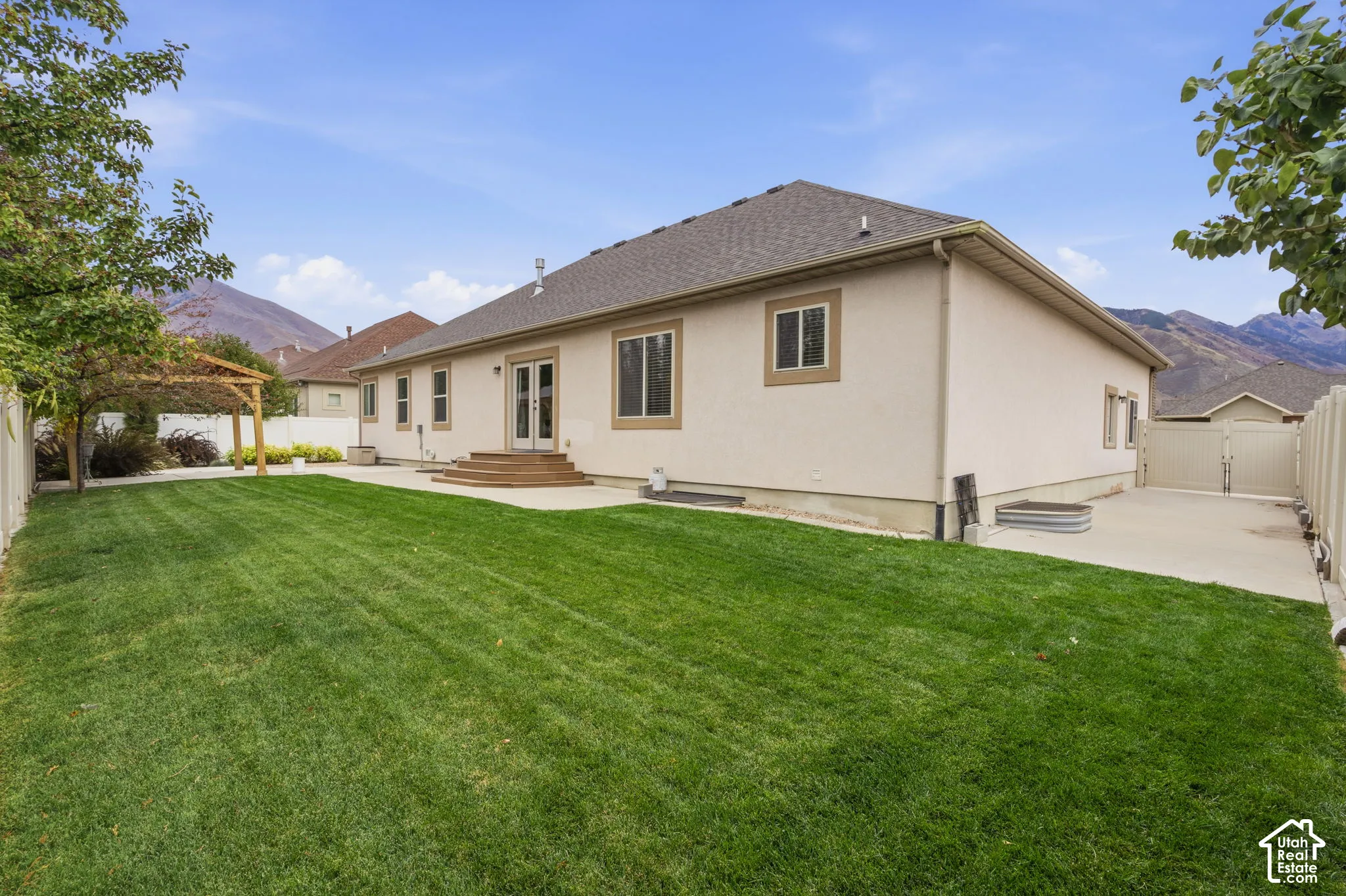 Rear exterior featuring a manicured lawn, concrete patio, wooden pergola, and mountain backdrop