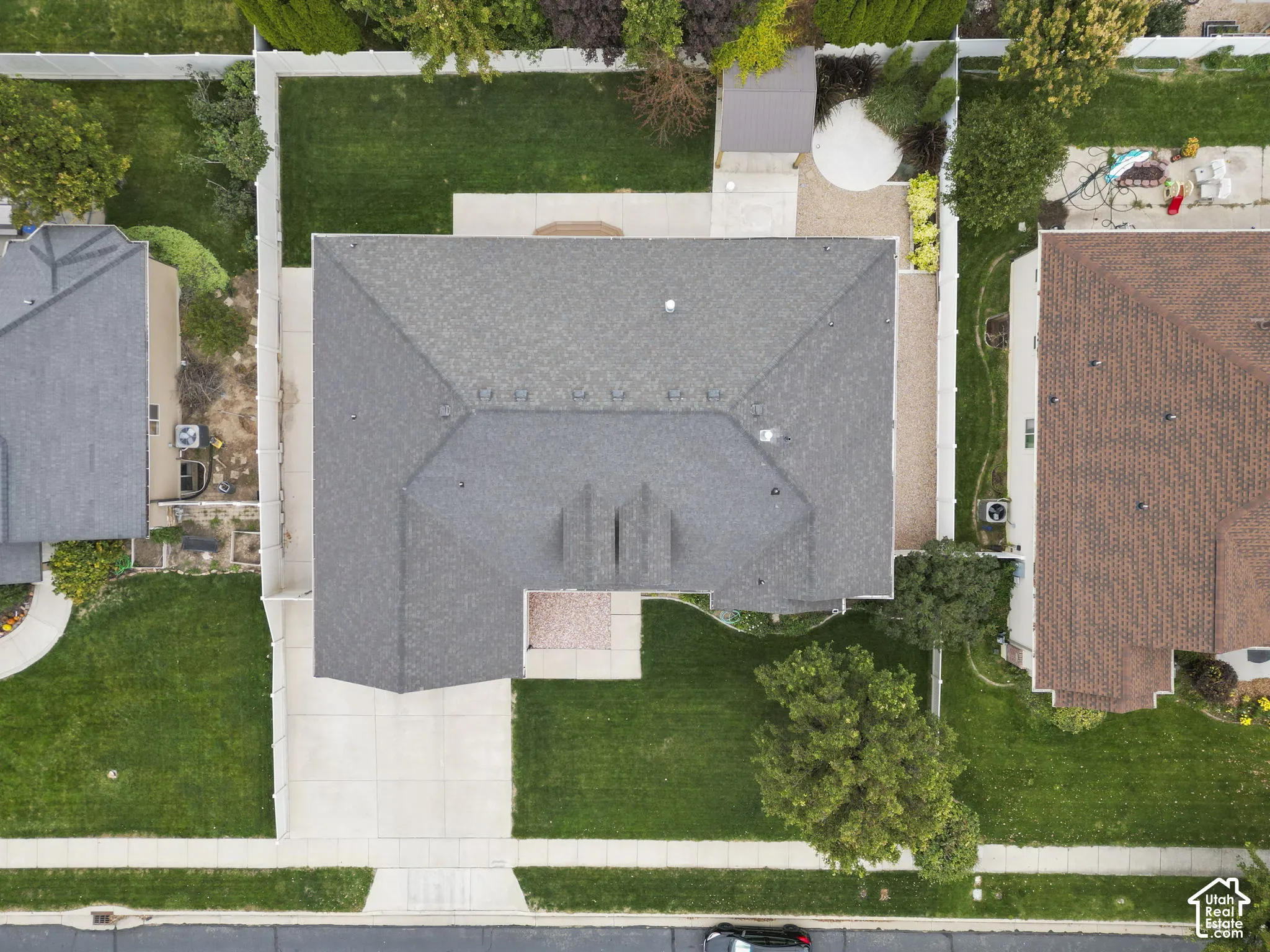Aerial perspective of a property featuring an expansive lawn, concrete driveway, fenced perimeter, shingle roof, and mature landscaping