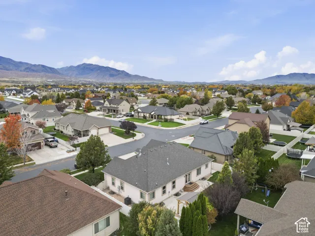 Aerial perspective of a suburban neighborhood featuring a light-colored stucco exterior, architectural shingle roofing, and a concrete rear patio, set against a prominent mountain backdrop