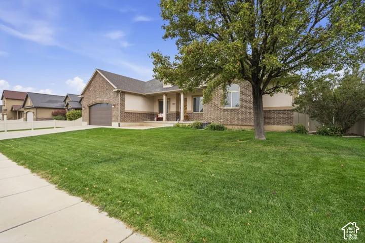 Brick and stucco exterior featuring a covered front porch with columns, an attached garage, and a expansive front lawn with mature trees