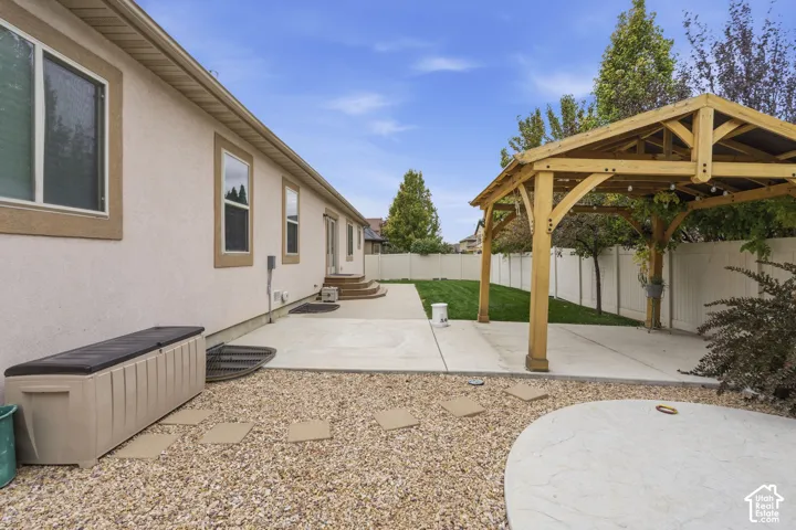 Backyard featuring a covered wood gazebo, concrete patio, lawn area, and gravel landscaping enclosed by vinyl fencing