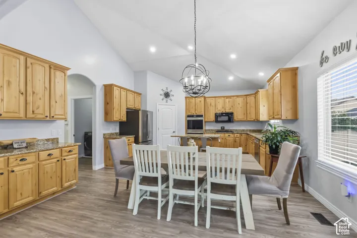 Kitchen featuring vaulted ceilings, wood-finish cabinetry, stone countertops, built-in double ovens, and a spherical metal chandelier