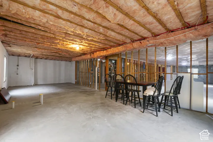 Unfinished interior space featuring exposed wood-frame stud walls, exposed ceiling joists with insulation, and concrete flooring