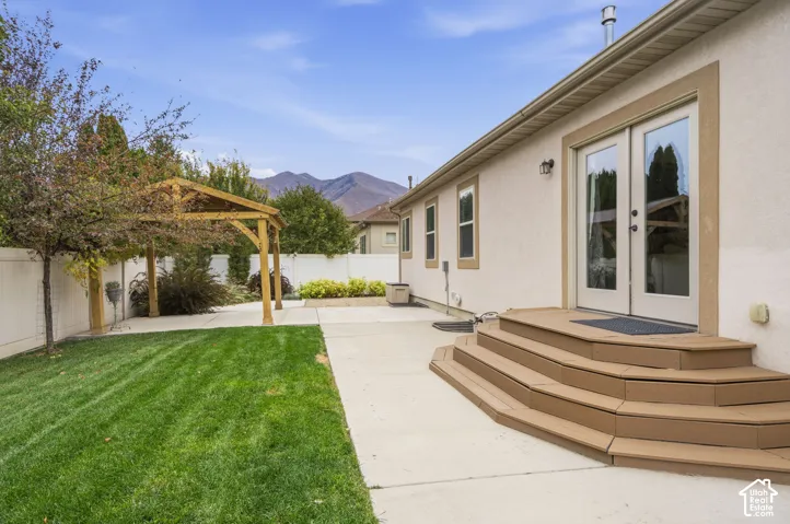 Stucco exterior featuring dual-pane windows and French glass patio doors with multi-tiered wood-finish stairs, concrete patio, detached timber-frame pergola, and mountain backdrop