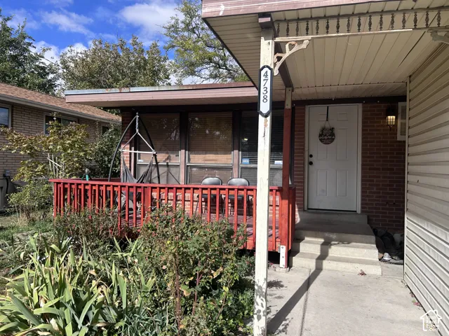 Exterior facade featuring red brick masonry, a covered porch with a painted wood railing, concrete steps, and a decorative eave bracket