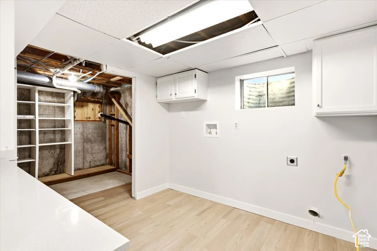 Laundry space featuring wood-finish flooring, built-in upper cabinetry, an exterior-facing window, and integrated shelving