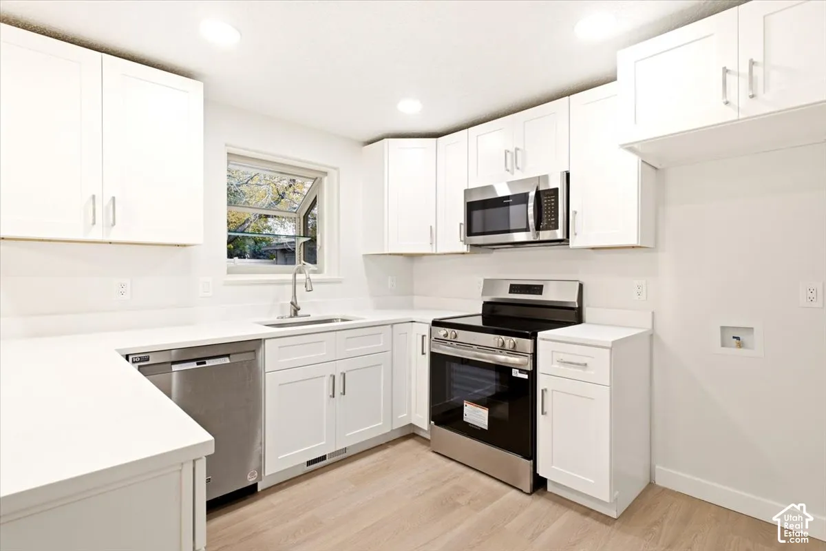 Kitchen featuring white cabinetry, solid-surface countertops, stainless steel appliances, and wood-finish flooring