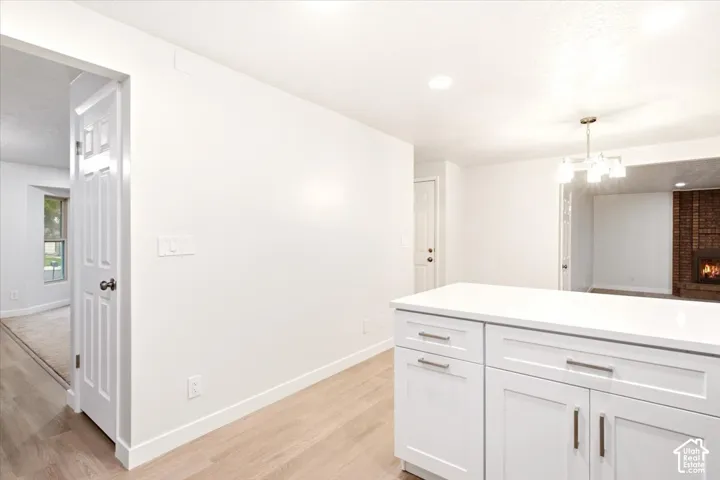 White cabinetry with minimalist hardware, quartz countertops, wood-finish flooring, and a multi-bulb chandelier