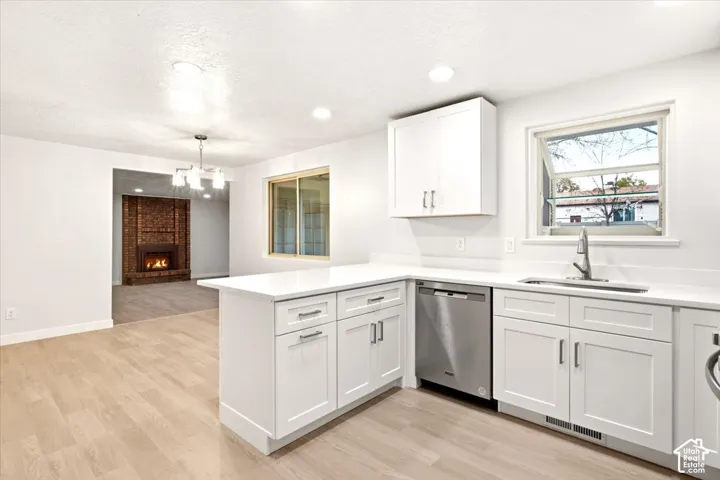 Kitchen featuring white shaker-style cabinetry, solid-surface countertops, recessed lighting, stainless steel dishwasher, and wood-finish flooring