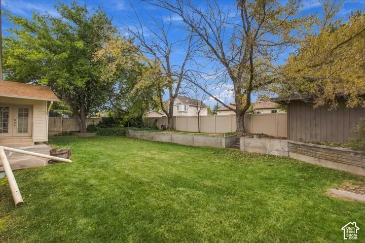 Backyard featuring a manicured lawn, concrete retaining walls, mature trees, and a perimeter privacy fence