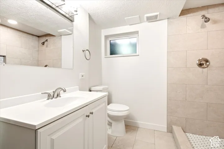 Bathroom featuring a white vanity cabinet with an integrated sink, polished metal faucet, large wall mirror, walk-in shower with neutral-toned wall tile and hexagonal floor tile, and a privacy window