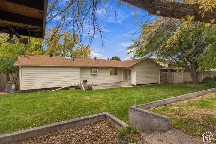 Backyard featuring a manicured lawn, concrete retaining walls, mature trees, and a concrete patio