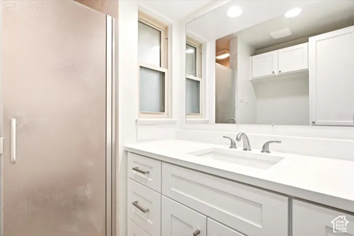Bathroom featuring a white cabinetry vanity with a solid surface countertop, undermount sink, chrome faucet, and expansive wall-mounted mirror