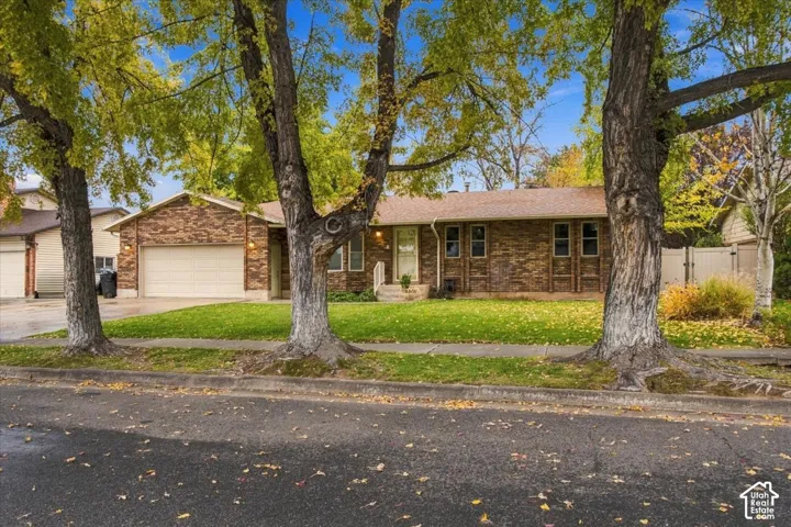 Rambler-style exterior featuring multi-toned brick masonry, an attached two-car garage, mature trees, and a front lawn