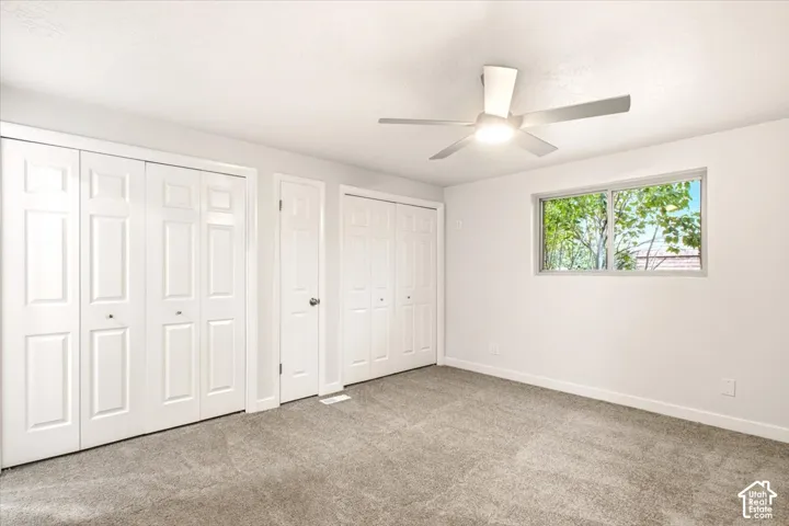 Neutral-toned carpeting, white six-panel closet doors, single swing door, and ceiling fan with integrated light fixture
