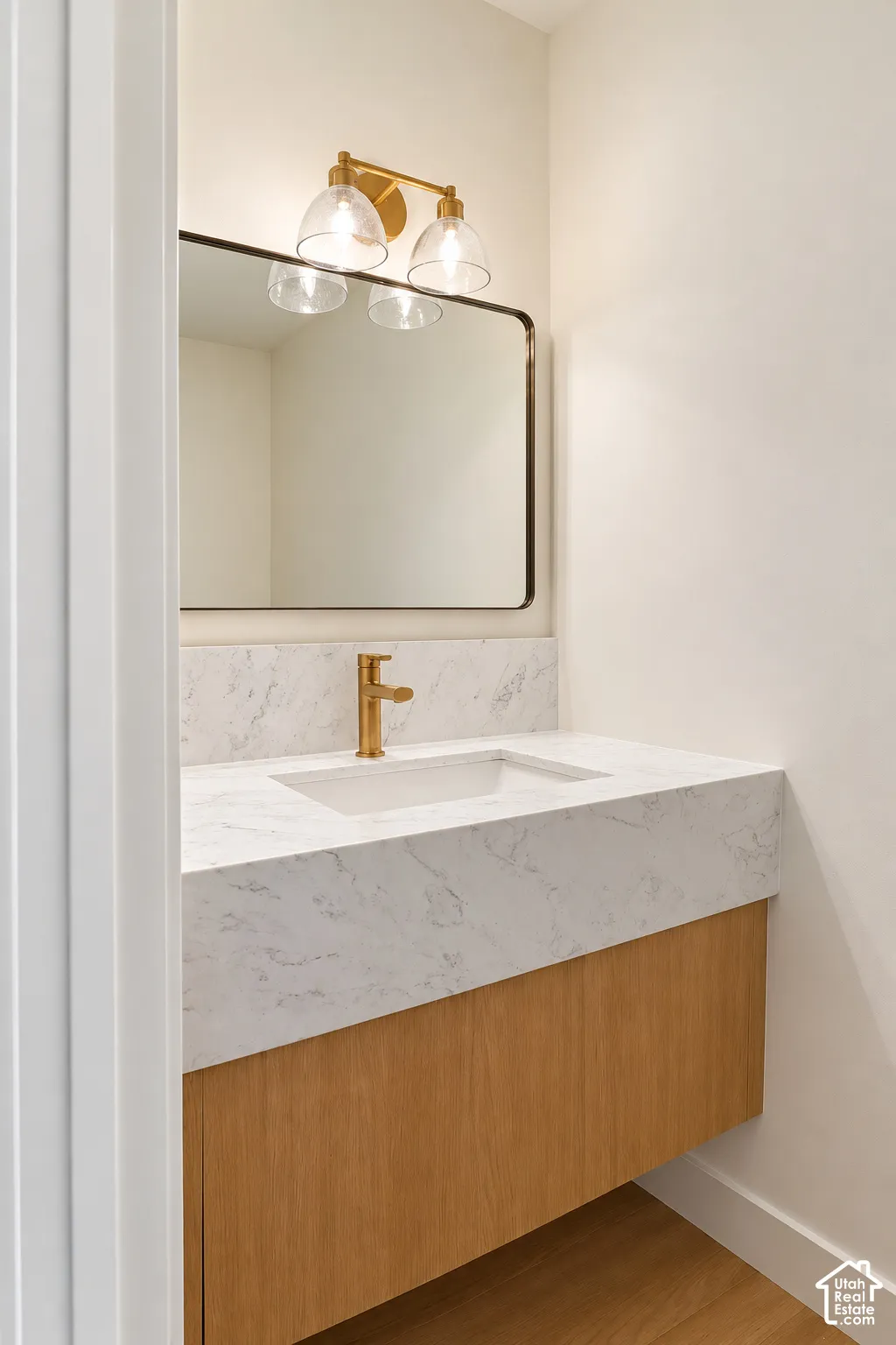 Floating wood-finish vanity with a stone-patterned countertop, integrated basin, brushed-gold faucet, rounded-corner mirror, and wall-mounted three-light fixture