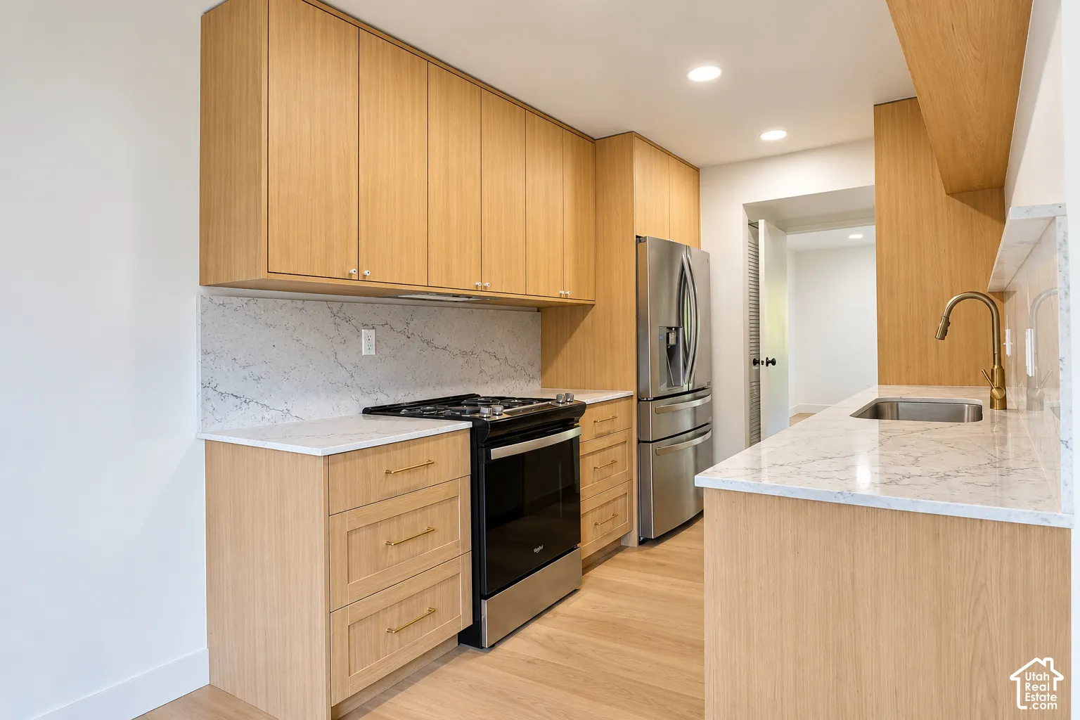 Kitchen featuring light wood-finish cabinetry, stone-style countertops, integrated stainless steel appliances, and gold-tone hardware