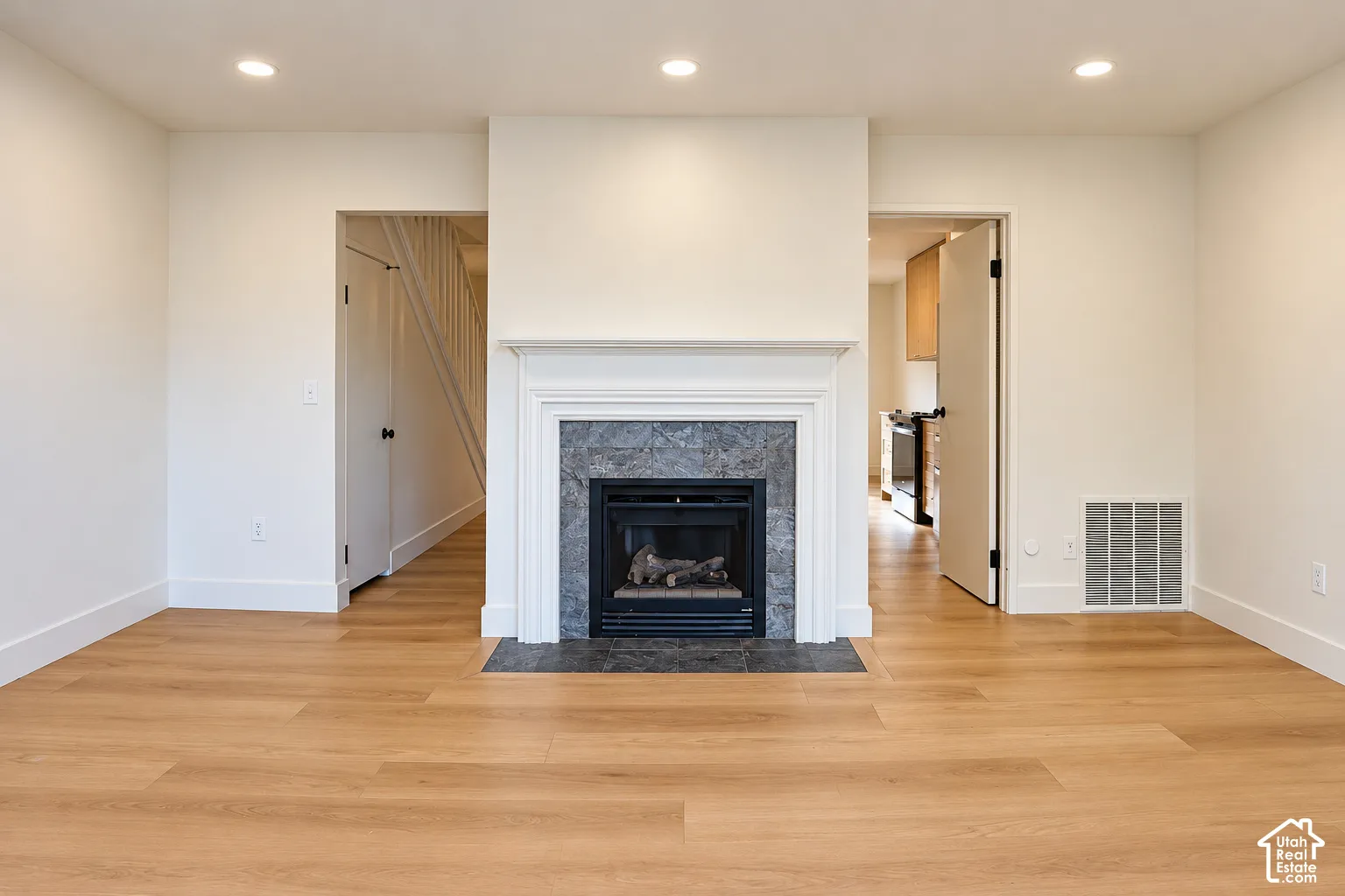 Fireplace featuring a classic white mantel, stone-tile surround, and dark hearth, complemented by recessed lighting and wood-finish flooring