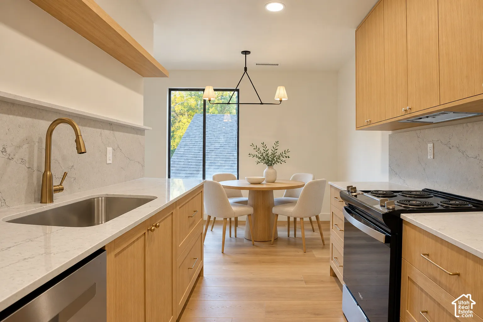 Kitchen featuring natural wood cabinetry, light-toned stone-finish countertops, full-height stone backsplash, wood-finish flooring, and a brass-tone gooseneck faucet Virtually Staged