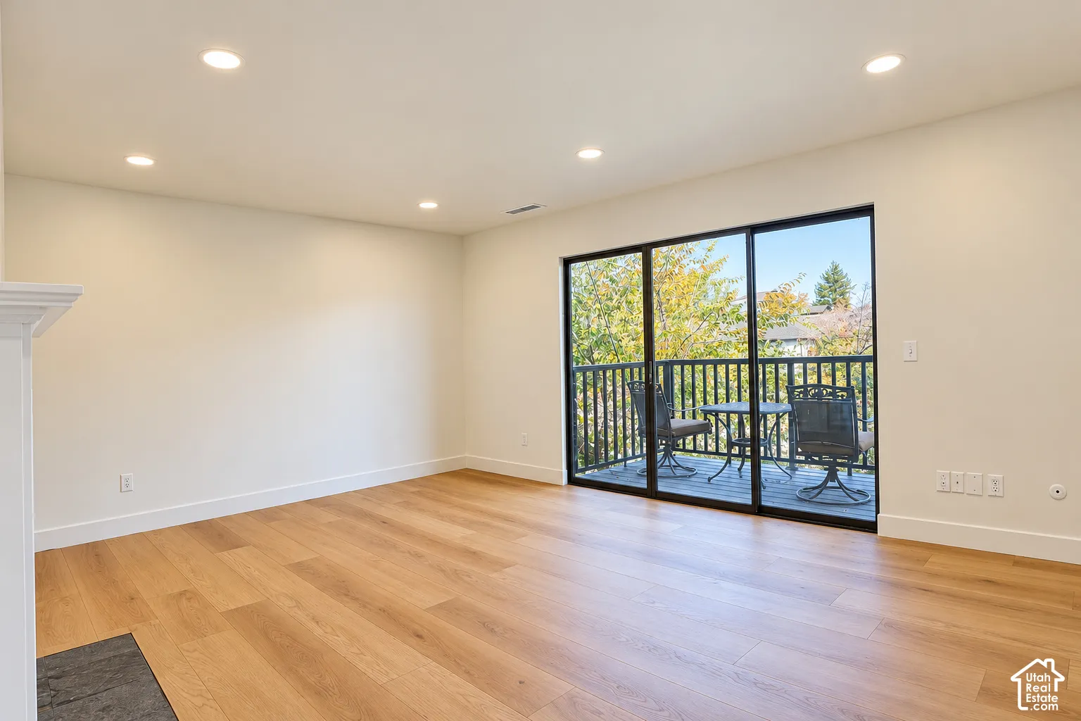 Open-concept room featuring wood-finish flooring, recessed lighting, and a sliding glass door providing access to a deck with black railing