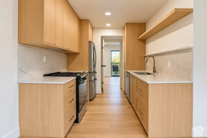 Kitchen featuring light-tone wood cabinetry, stone-surface countertops, full-height stone backsplash, recessed lighting, and floating wood shelving