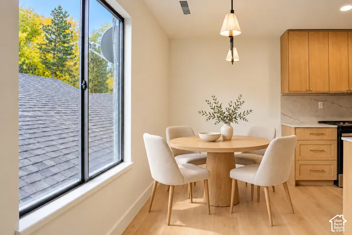 Kitchen area featuring light-finish wood cabinetry, stone-style countertops, wood-finish flooring, large window, and dual-shade pendant lighting. Virtually Staged.
