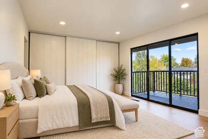 Sliding glass doors with black frames opening to an exterior balcony, wood-finish flooring, floor-to-ceiling sliding closet doors, and recessed lighting Virtually Staged
