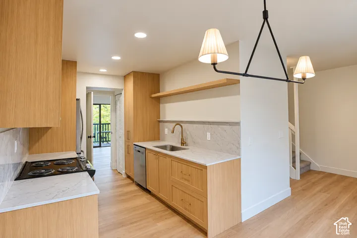 Kitchen featuring light-tone flat-panel cabinetry, stone-surface countertops, integrated stainless steel appliances, floating wood shelf, and brushed metal faucet