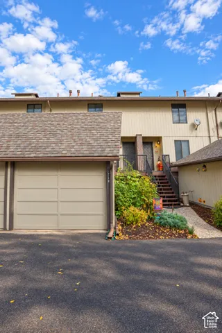 Multi-level exterior featuring tan vertical siding, asphalt shingle roofing, an integrated garage with a paneled door, and a staircase with metal railings