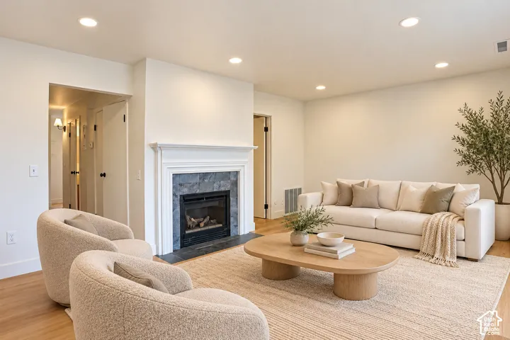 Living area featuring wood-finish flooring, recessed lighting, and a fireplace with a stone surround and a white mantle Virtually Staged